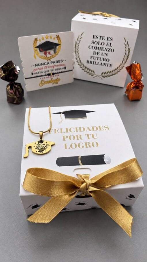 Inicio Collar dorado con dije de birrete «Prom 2026» sobre la caja de grado «Felicidades por tu logro», con su manilla y chocolates